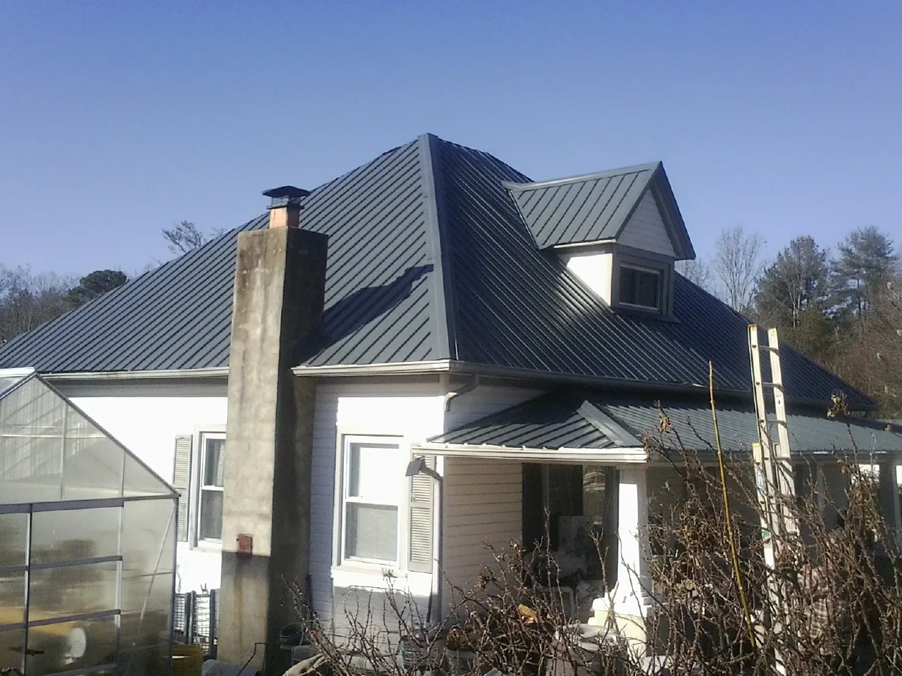 Dark blue standing seam metal roof on a white farmhouse with dormer — Slate & Tile Roof Repair by Roofing Brothers in Sheyenne