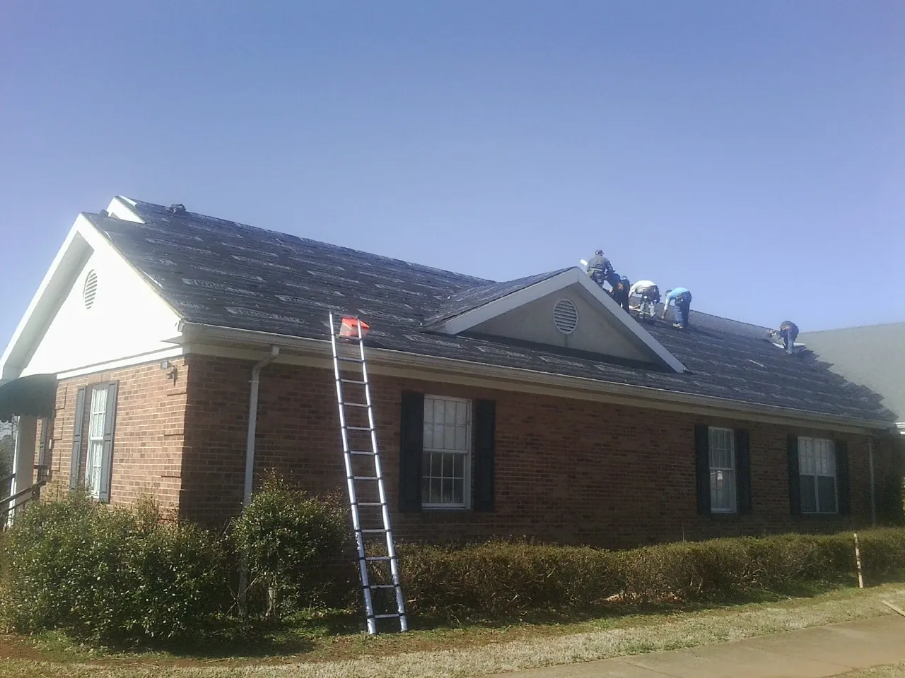 Crew tearing shingles off a brick ranch roof with a ladder set — Emergency Roof Repair work by our crew in Sheyenne