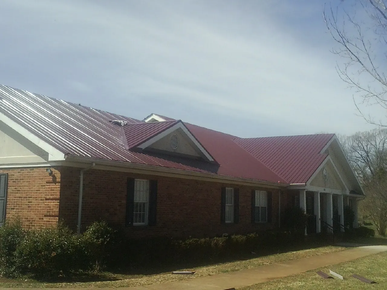 Red metal roof with gabled entries on a long brick building, from a Hail Damage Roof Repair job in Sheyenne