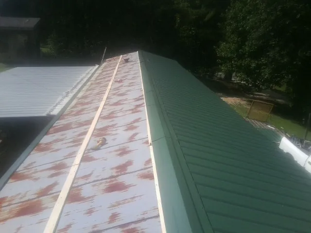 Old rusted panels beside newly installed green metal roofing — Wind Damage Roof Repair by Roofing Brothers in Sheyenne