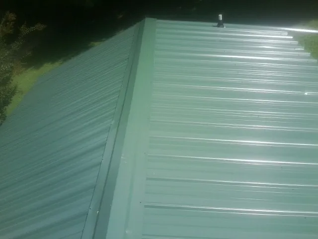 New green metal panels meeting at the ridge of a roof — Flat Roof Repair work by our crew in Sheyenne