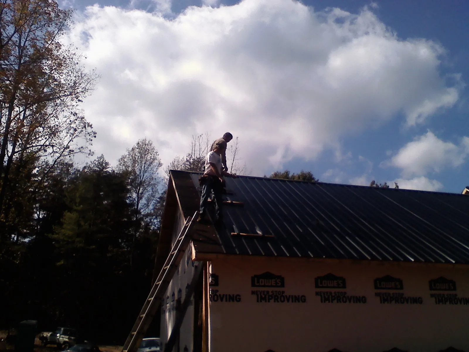 Roofer fastening dark metal panels high against a cloudy sky, from a Roof Inspection job in Sheyenne