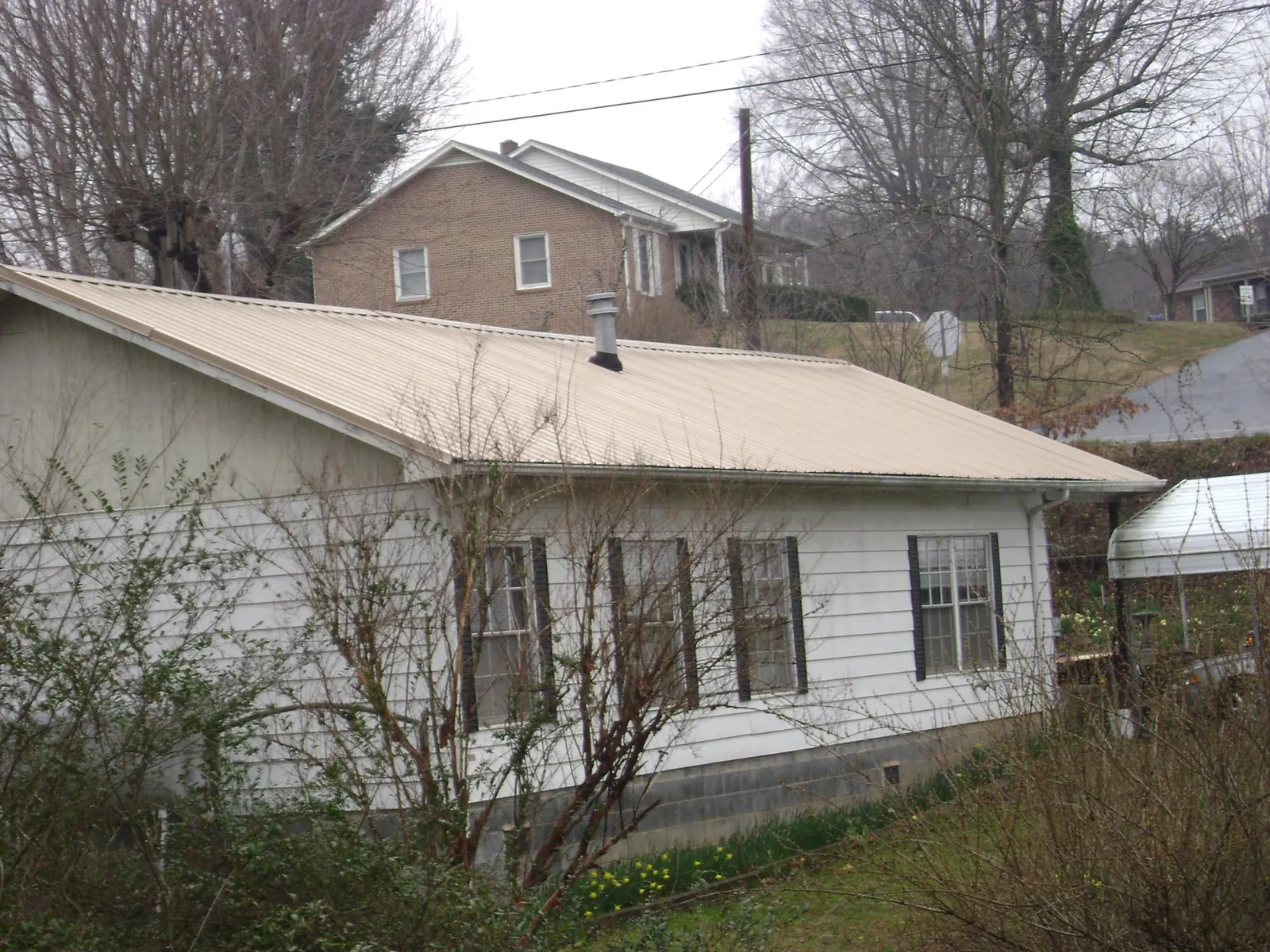 Tan metal roof on a white sided house set into a hillside — Commercial Roofing by Roofing Brothers in Sheyenne
