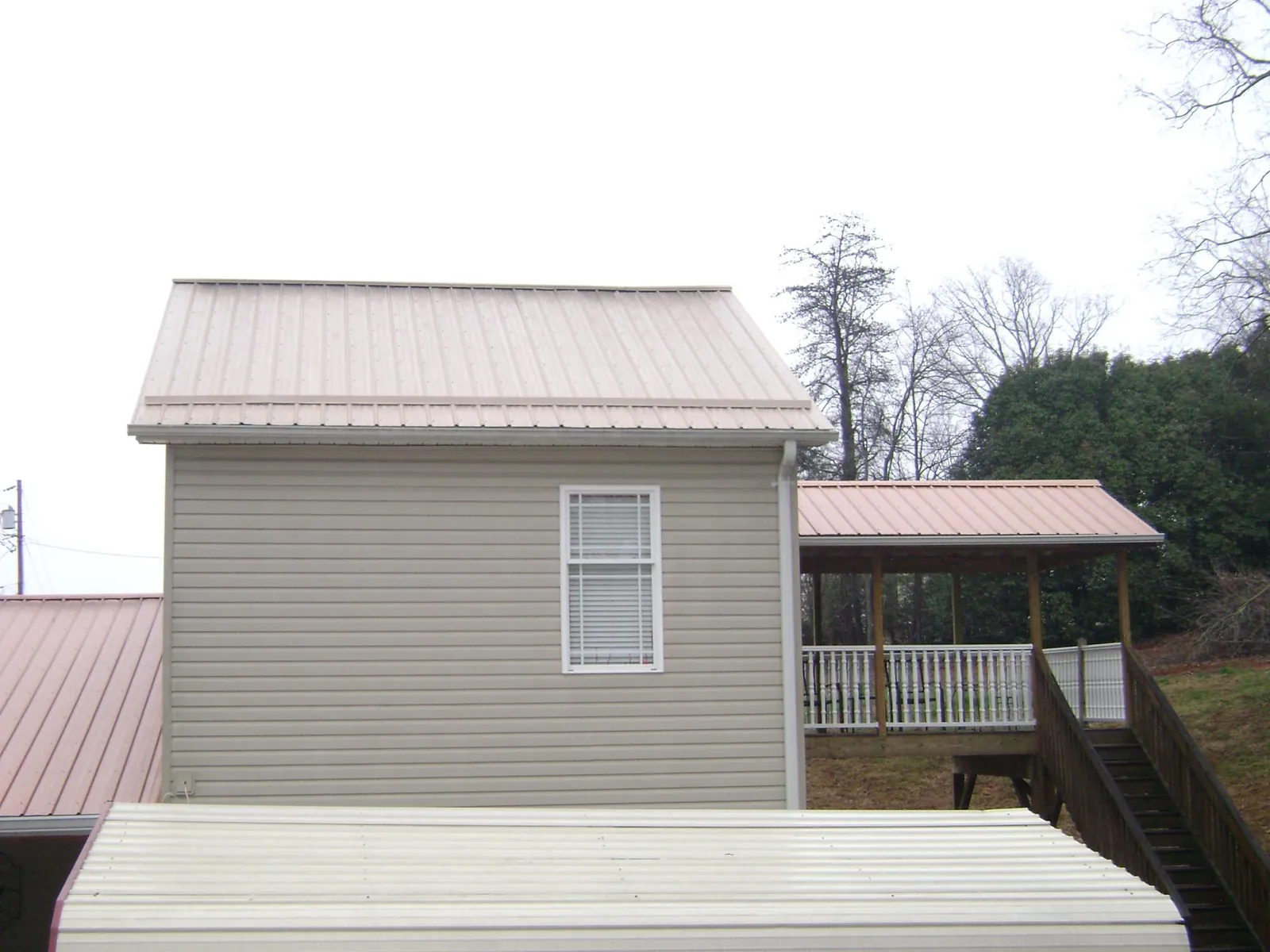 Tan metal roofs on a two story addition and attached porch, from a Roof Replacement job in Sheyenne